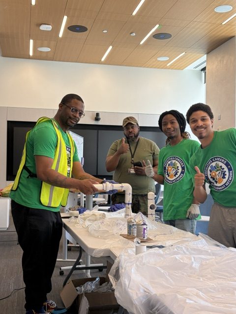 Trainees giving a thumbs up over the piping assembly they built